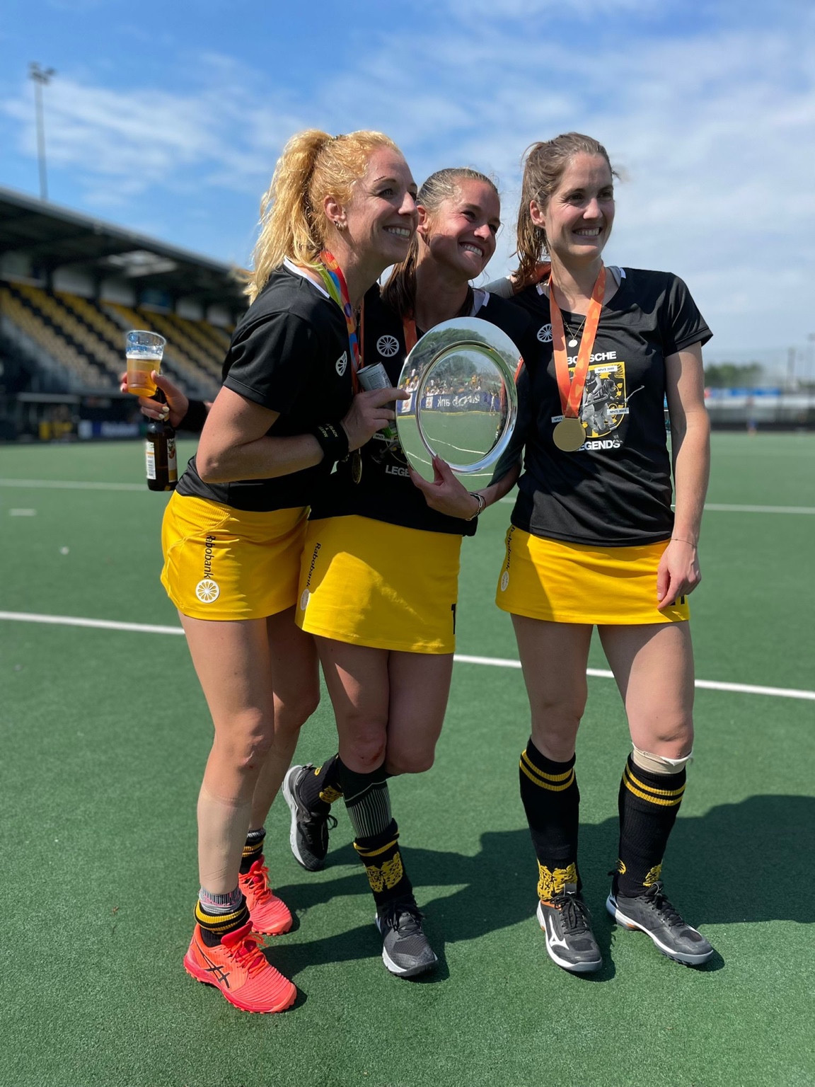 Lidewij Welten, in het midden, met twee hockeysters en een schaal op het hockeyveld.